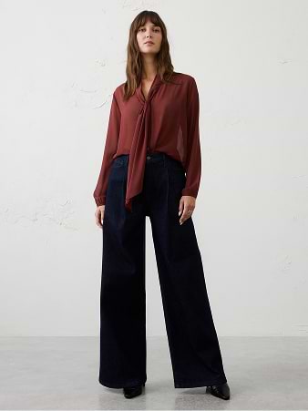Person wearing a burgundy tie-neck blouse and wide-leg navy trousers, standing against a plain light background.