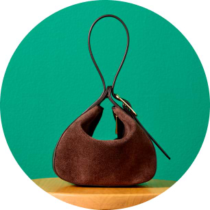 Brown suede handbag with a looped strap on a wooden table, teal background.
