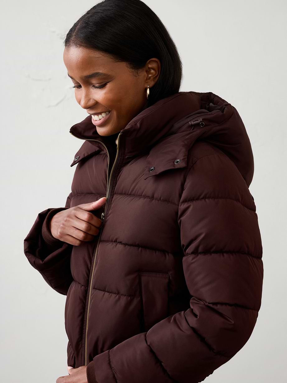 Person smiling while zipping a dark maroon hooded puffer jacket.