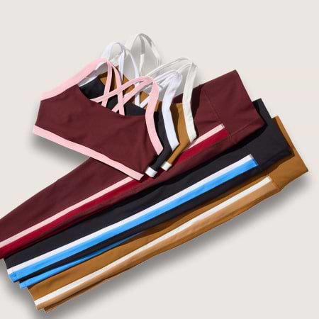 Assorted strappy sports bras and matching leggings in burgundy, black, mustard, and blue, folded flat.