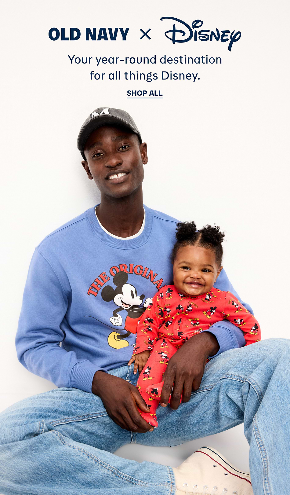 Old Navy x Disney ad showing a smiling adult in a blue Mickey Mouse sweatshirt holding a smiling toddler in a red Mickey onesie, with headline: “Your year-round destination for all things Disney.”