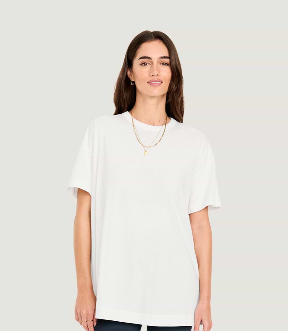 Person wearing an oversized white T-shirt with layered gold necklaces against a light gray background.