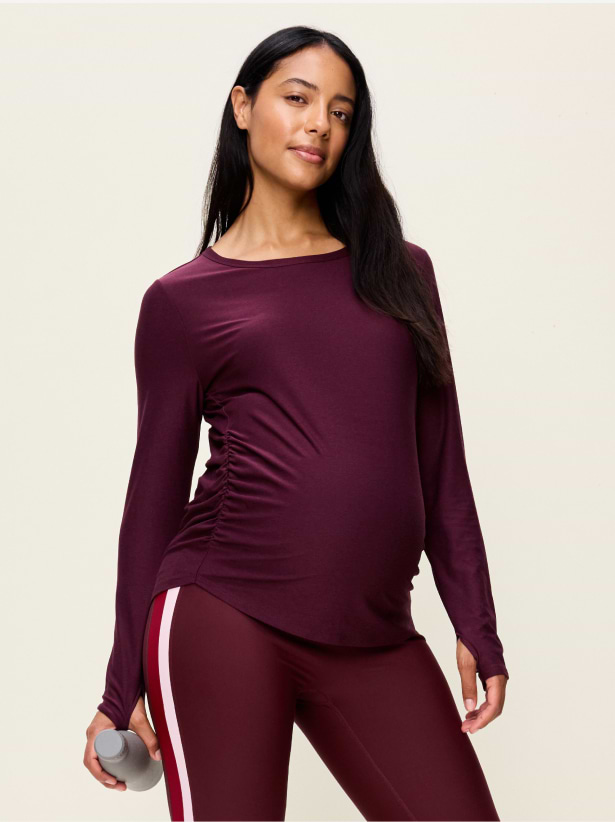 Person in burgundy long-sleeve ruched top and maroon striped leggings, holding a small dumbbell.