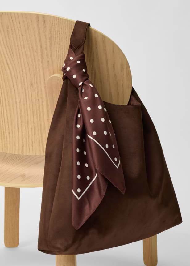 Brown shoulder bag hanging on a light wooden chair, with a brown-and-white polka dot scarf tied to the handle.