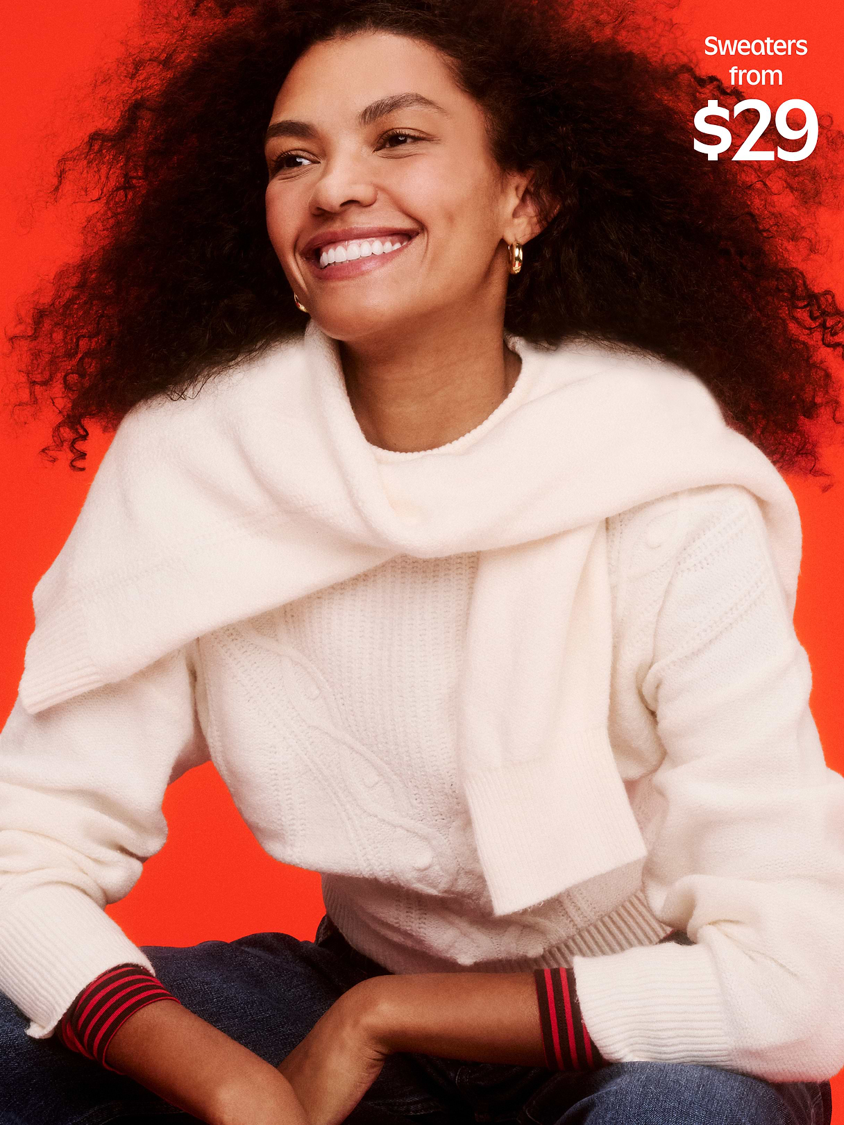 Smiling person in a white knit sweater with a matching wrap, red background; text reads “Sweaters from $29.”