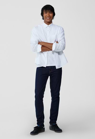 A male model wearing skinny jeans and a light denim button-down shirt.
