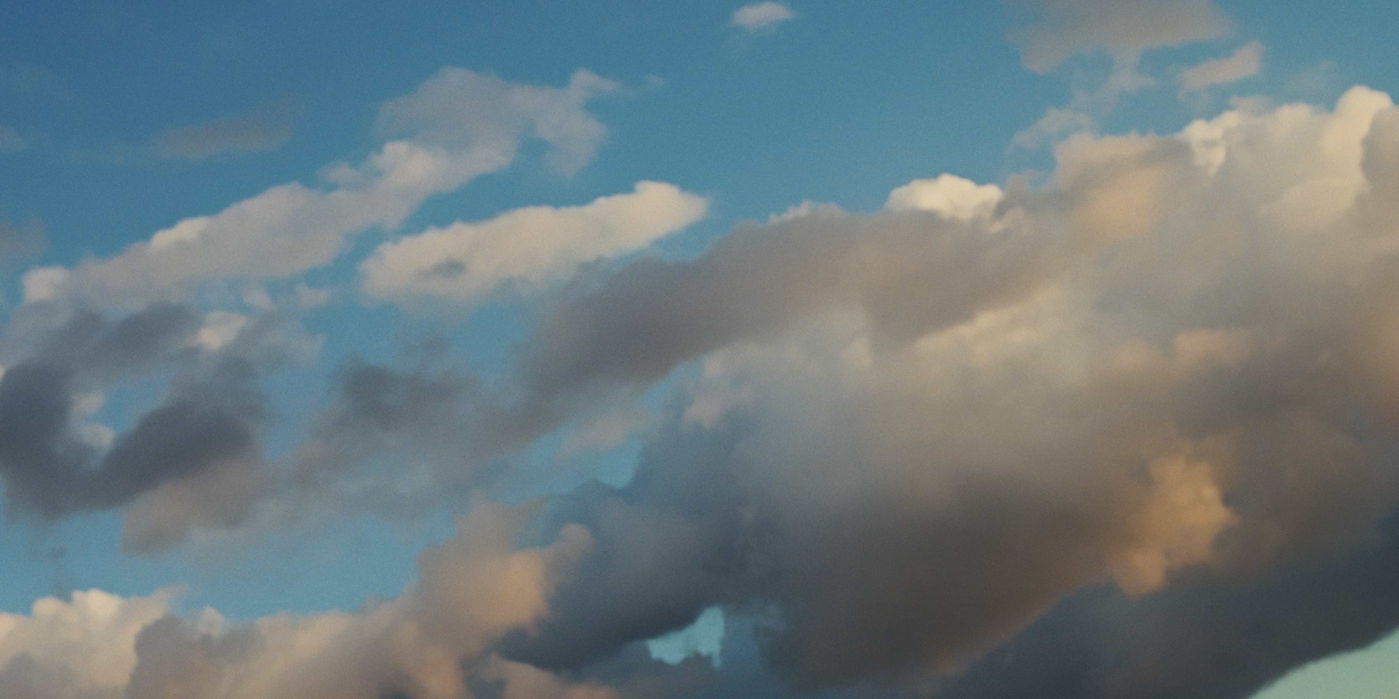 Alt text: Blue sky with layered clouds—some dark, others warm-lit—suggesting evening light.