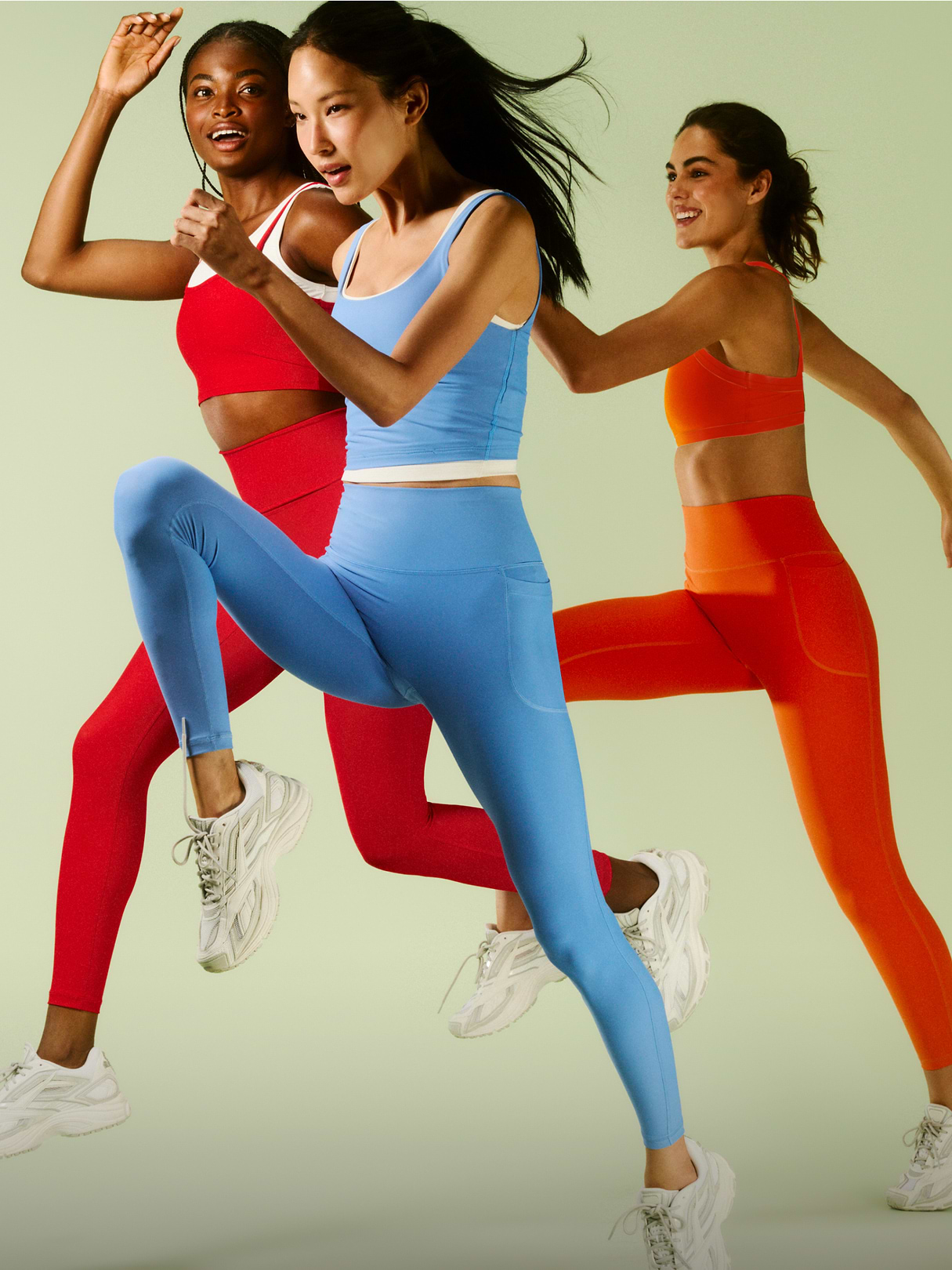 Three people in red, blue, and orange workout sets mid-run against a pale green background.