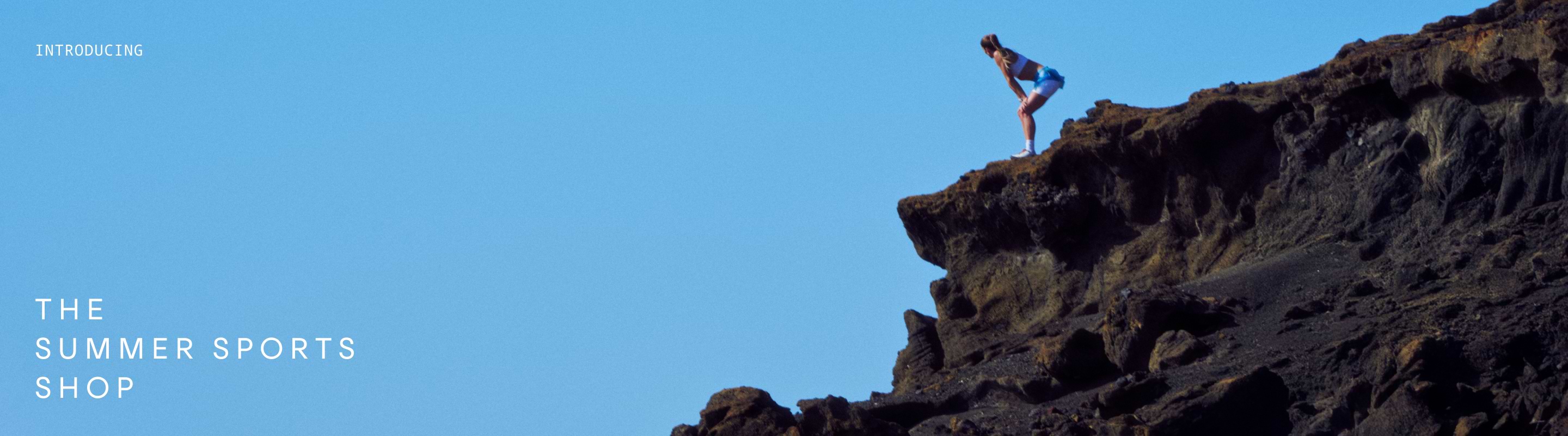 Person in athletic wear standing on the edge of a rocky cliff under a clear blue sky.