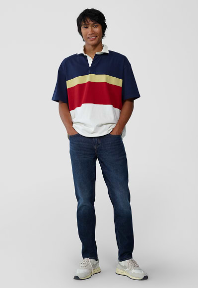 A male model wearing athletic taper jeans and a white t-shirt and navy cardigan.