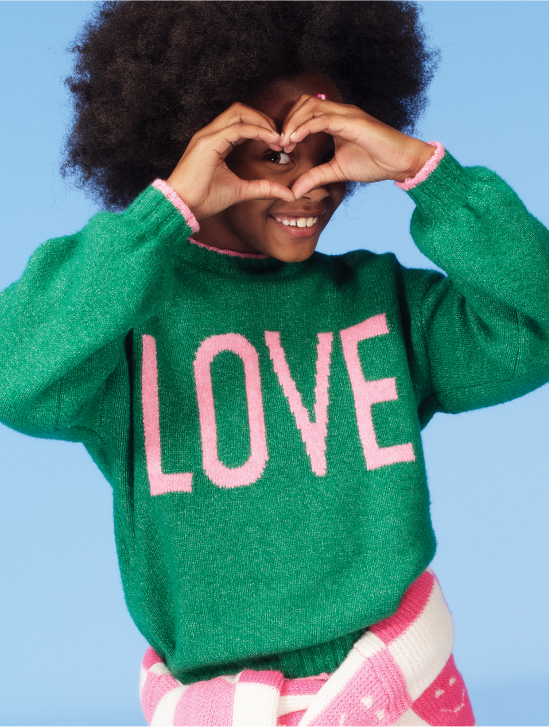 Image of a young girl model wearing a green graphic sweater.