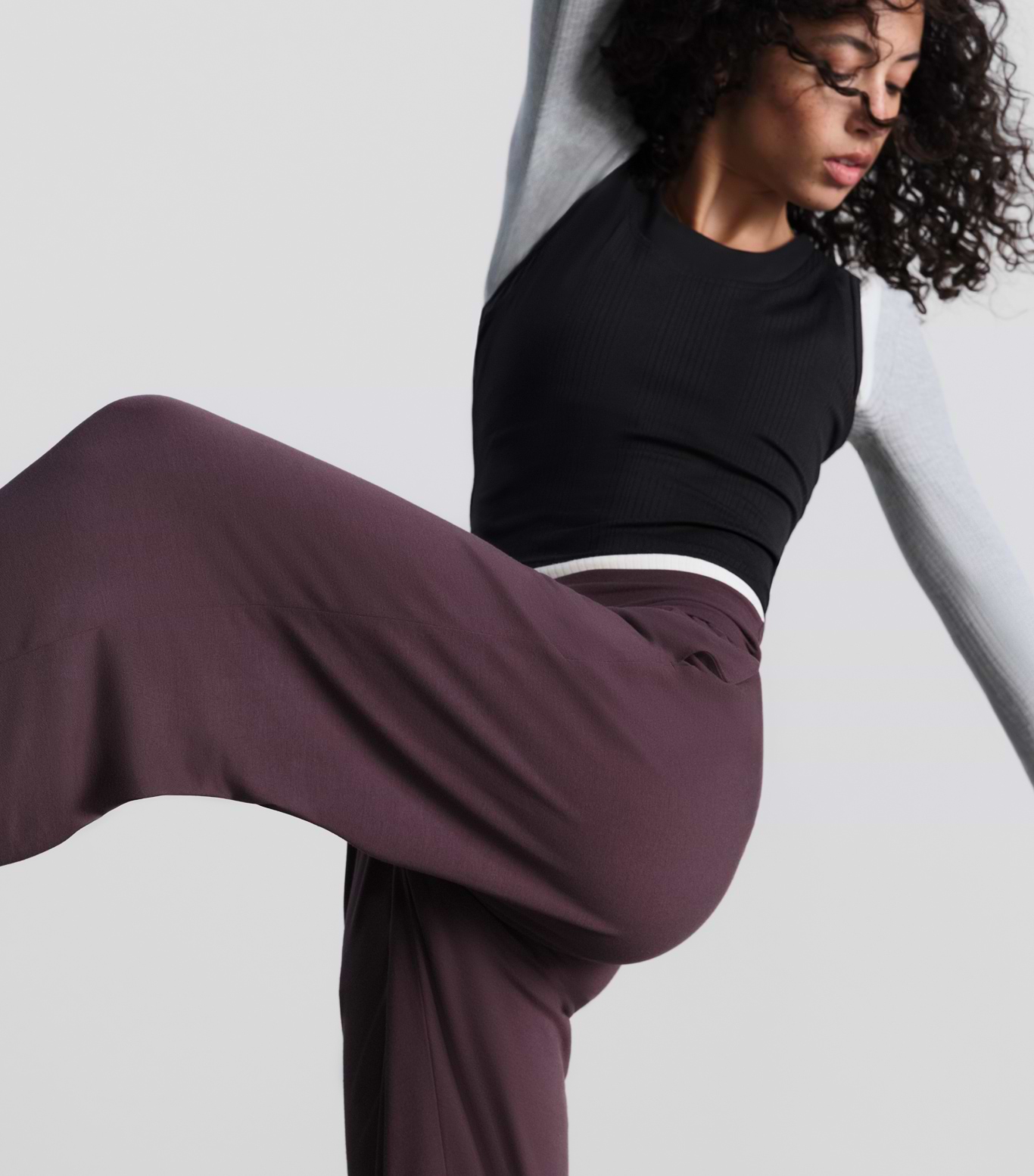 Person in motion lifting one leg, wearing flowy plum pants and a black-and-gray top.
