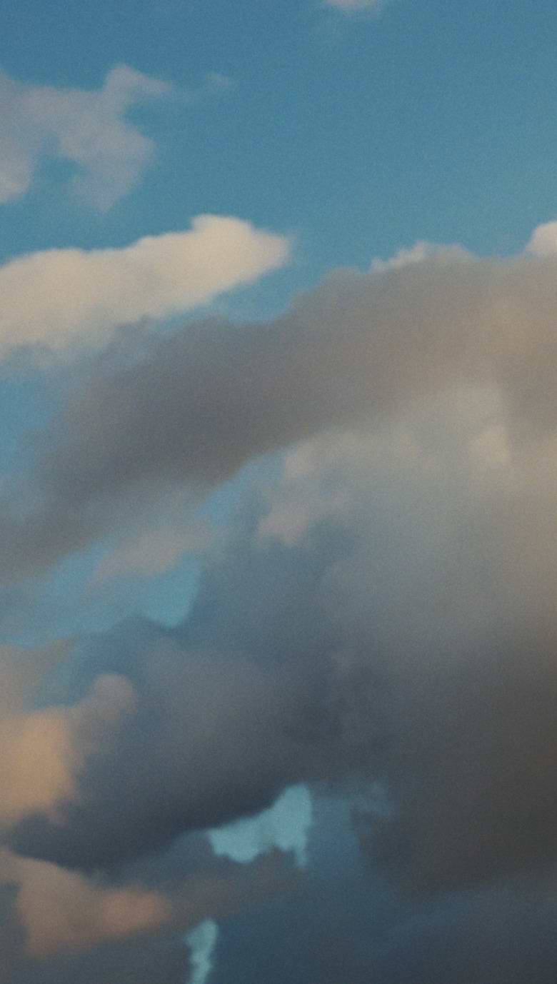 Blue sky with large gray and white clouds softly lit by sunset.