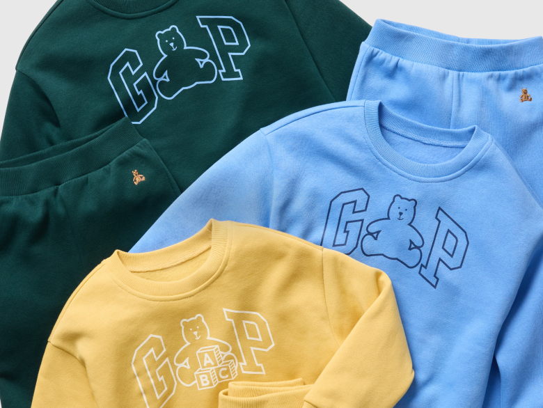 Flat lay of kids’ sweatshirts and joggers in green, blue, and yellow with GAP bear graphics.