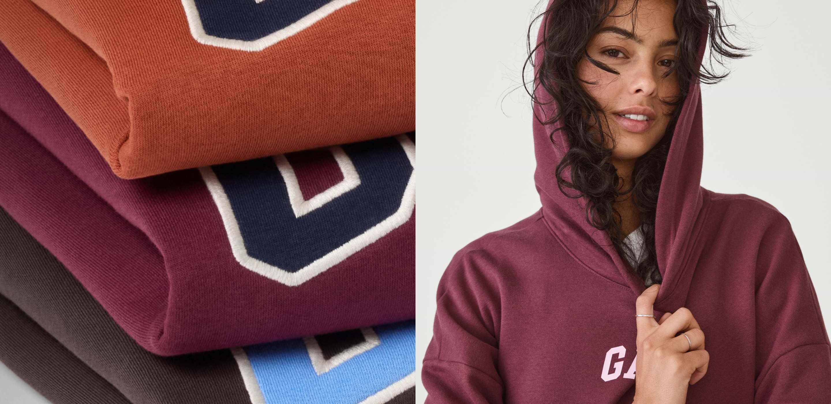 Stack of folded sweatshirts in rust, burgundy, and blue with varsity letters; next to them, a person wearing a burgundy hoodie with the hood up.