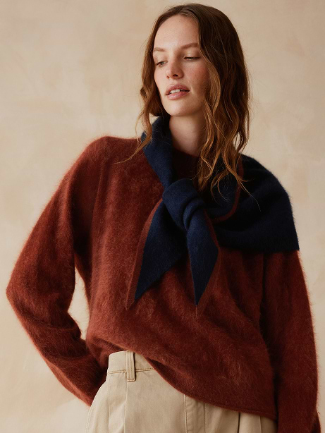 Person in a rust fuzzy sweater with a navy scarf tied over the shoulders and beige pants, against a neutral background.
