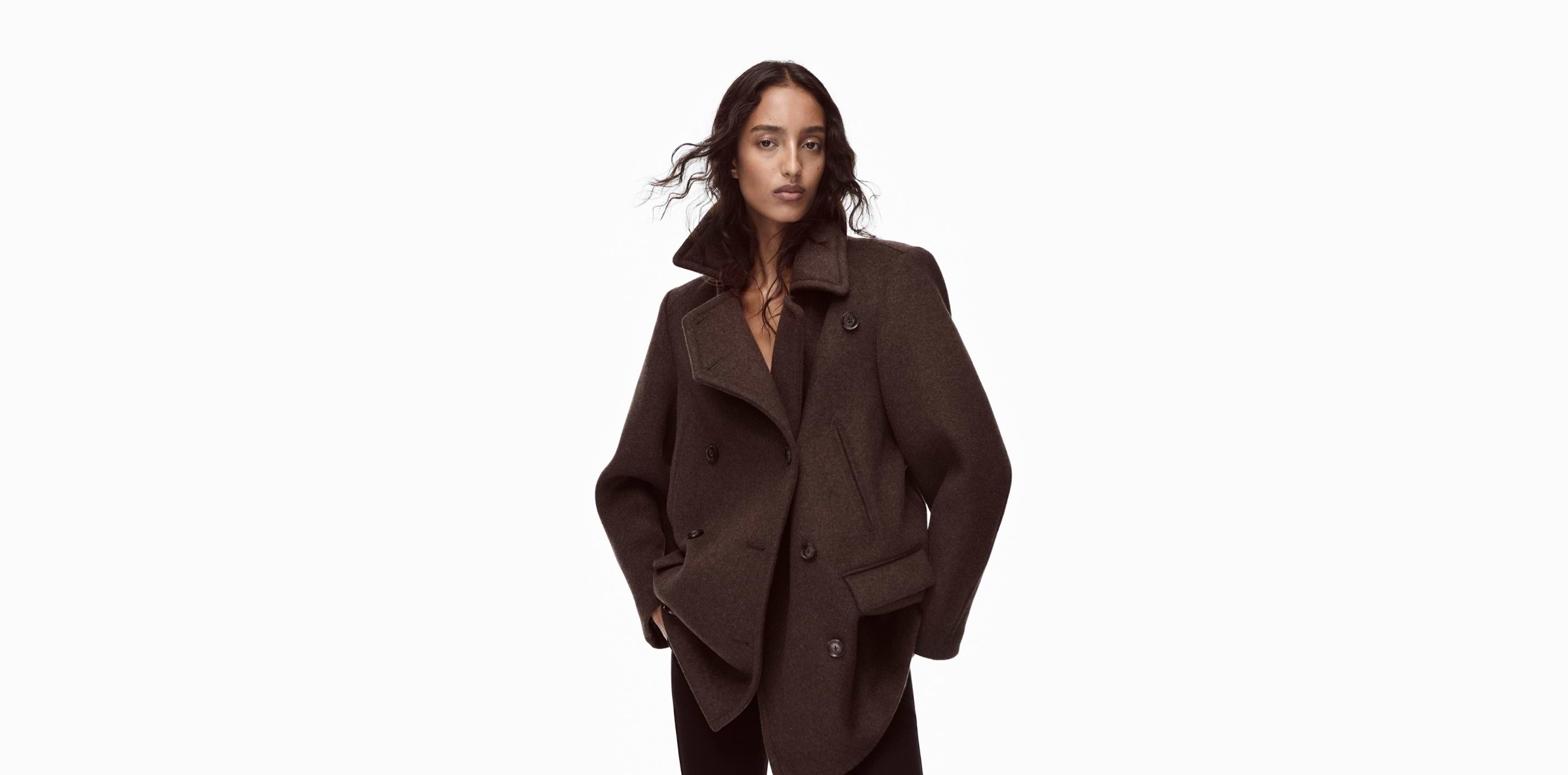 a woman in a brown jacket standing in front of a white background