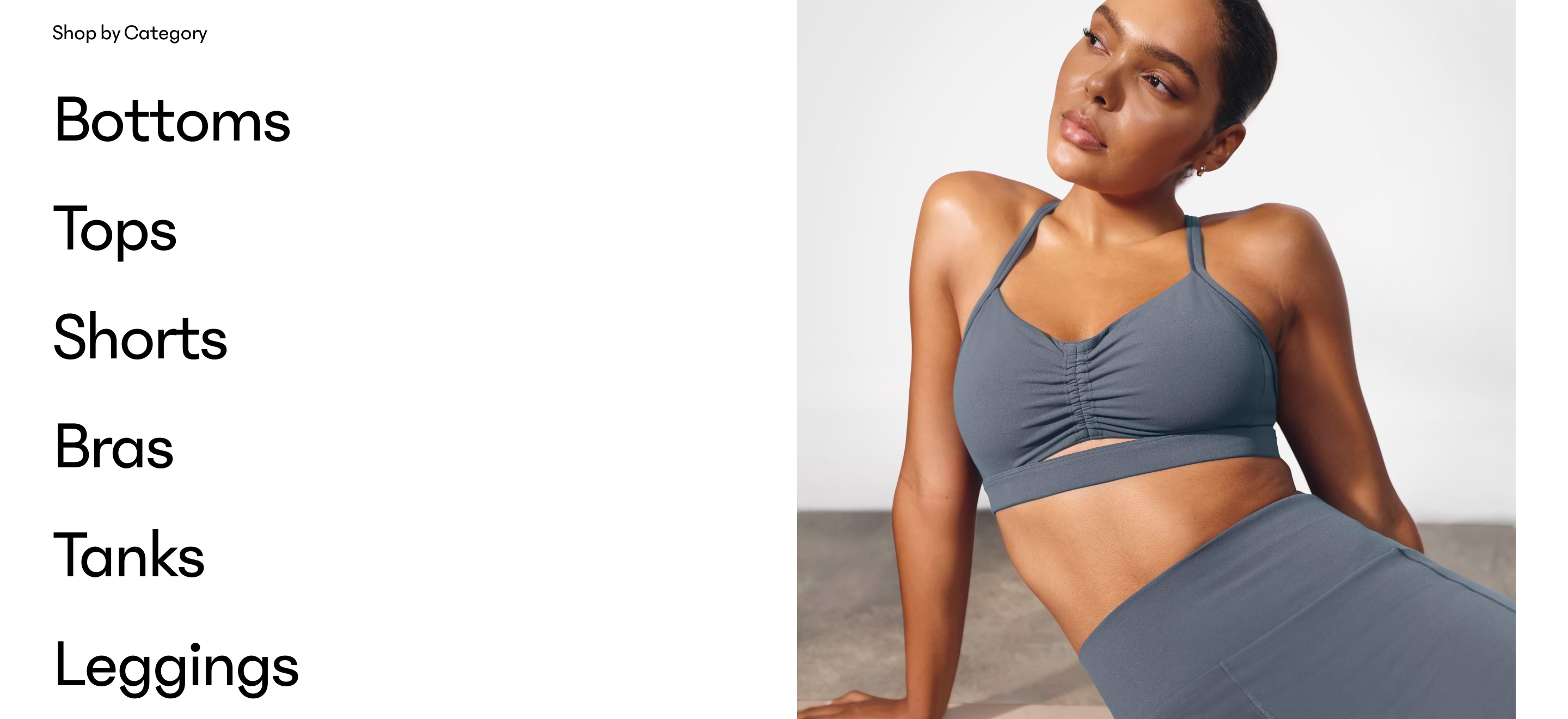Shop by Category list—Bottoms, Tops, Shorts, Bras, Tanks, Leggings—beside a model reclining in slate-gray sports bra and leggings.