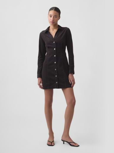 Person wearing a black long-sleeve button-front mini shirt dress and black heeled sandals, standing against a plain background.