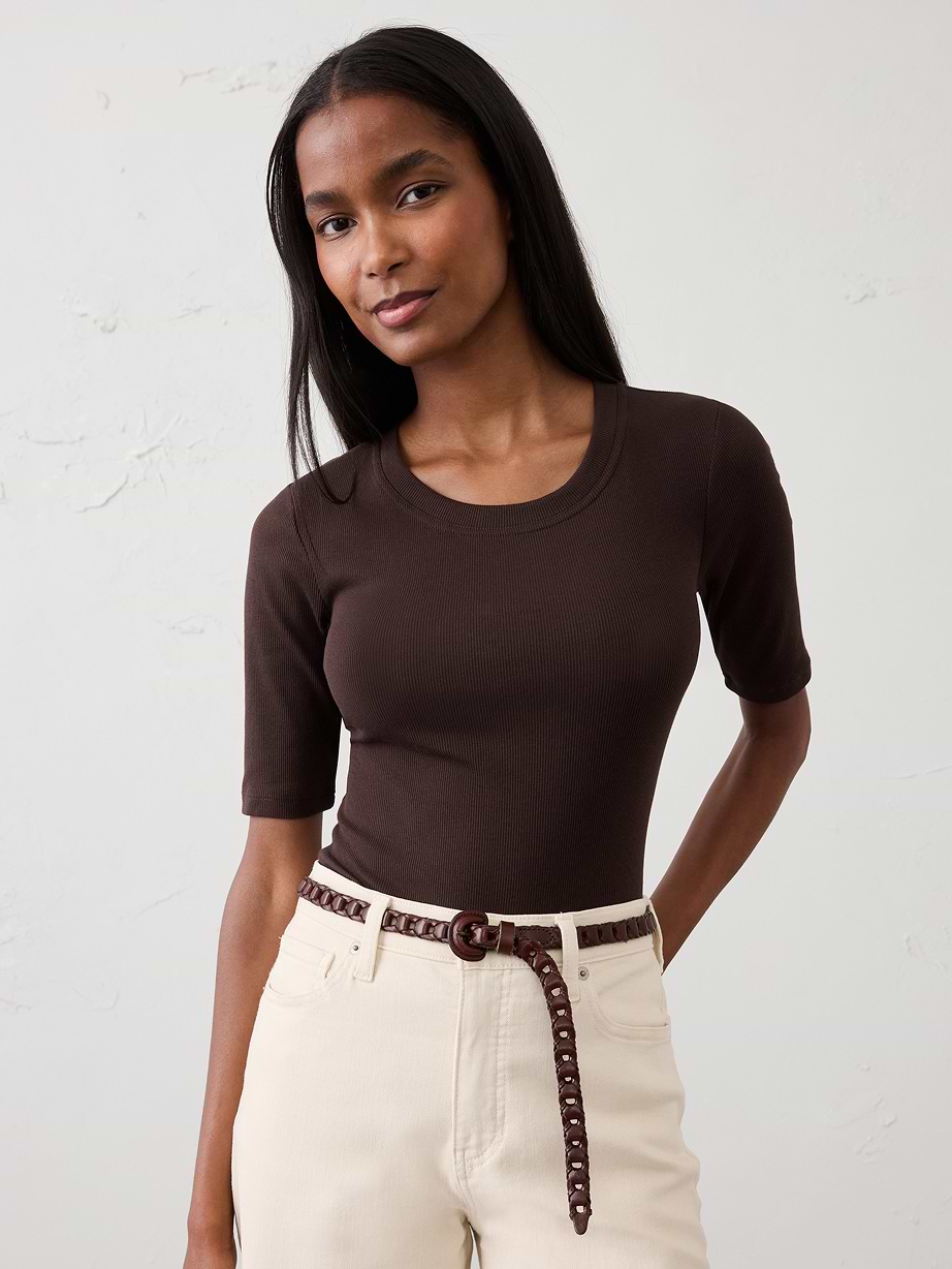 Person wearing a fitted dark brown short-sleeve top with cream high-waisted jeans and a brown woven belt.