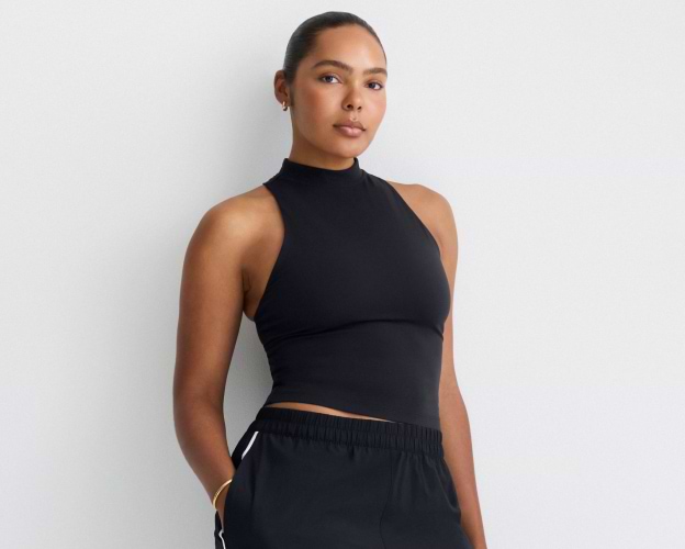 Person wearing a black high-neck sleeveless top and black joggers against a plain background.