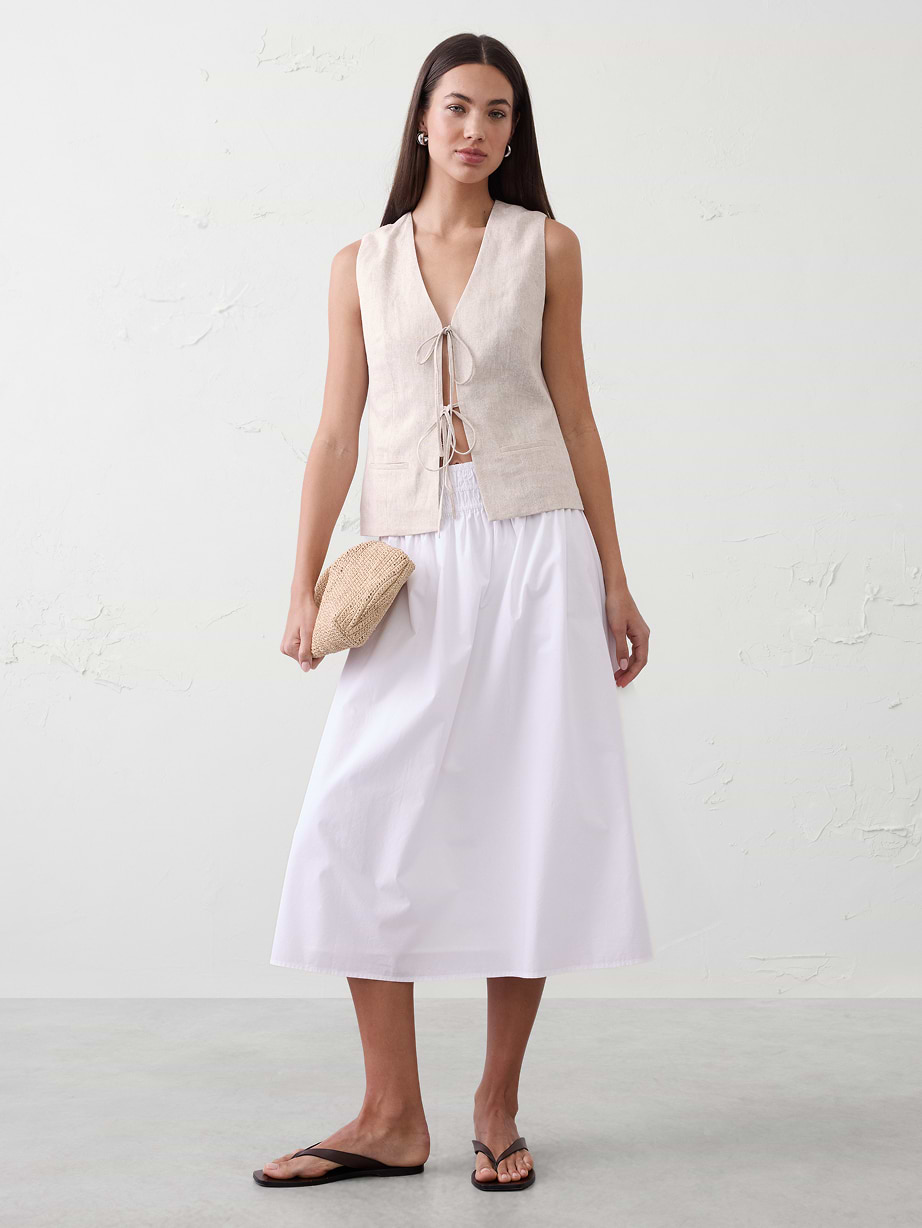 Woman in tan top and white skirt. 
