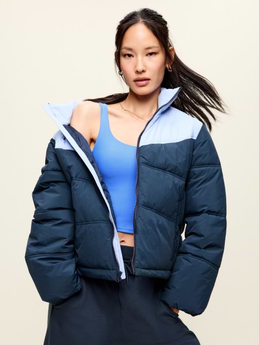Person wearing a navy puffer jacket with a light blue yoke, unzipped over a blue sports bra.