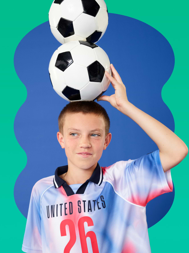 Young FIFA fan balancing three soccer balls on his head.