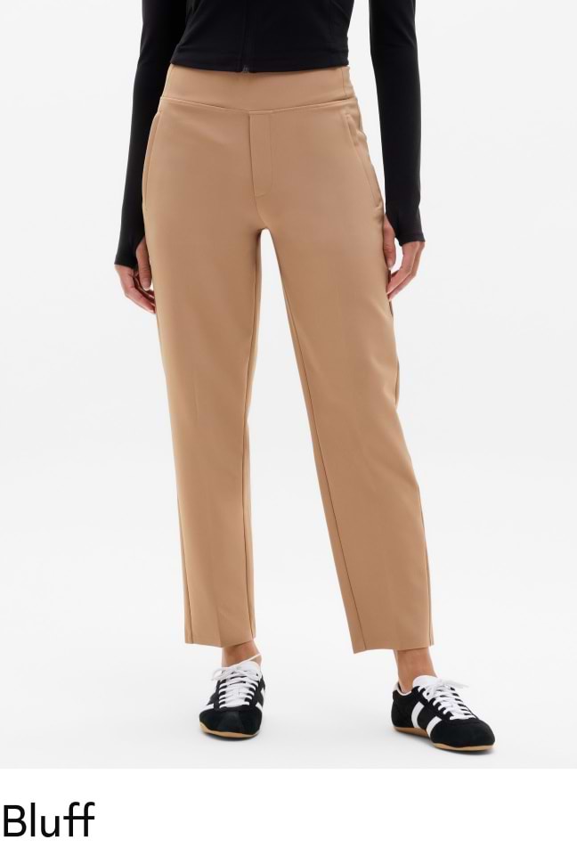 Person wearing tan, straight‑leg ankle pants, paired with a black long‑sleeve top and black sneakers with white laces.