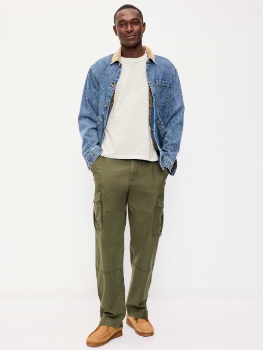 Person standing against a white background wearing a denim jacket over a white T-shirt, olive cargo pants, and tan shoes.