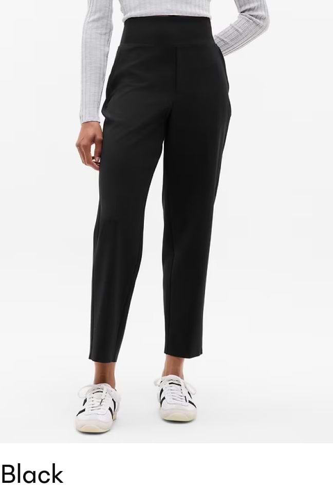 Model wearing black high-waisted tapered ankle-length trousers with white sneakers.