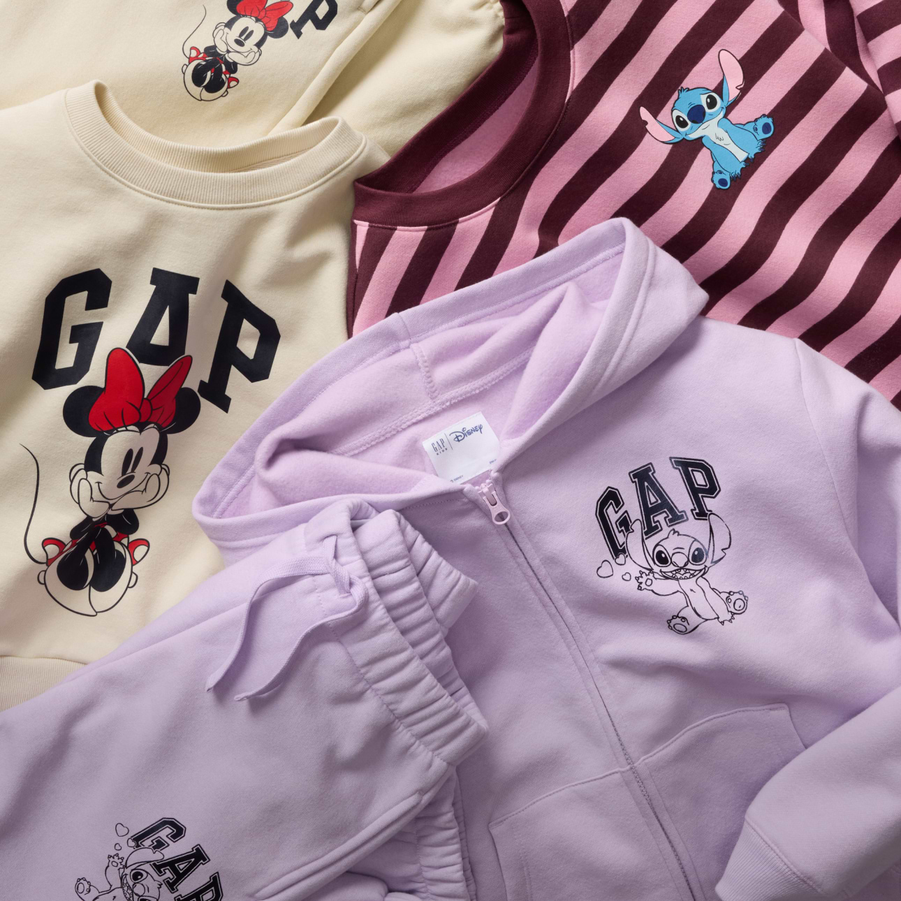 GAP x Disney clothing flat lay: cream sweatshirt with Minnie Mouse, pink striped top with Stitch, and lilac hoodie and joggers with Stitch.