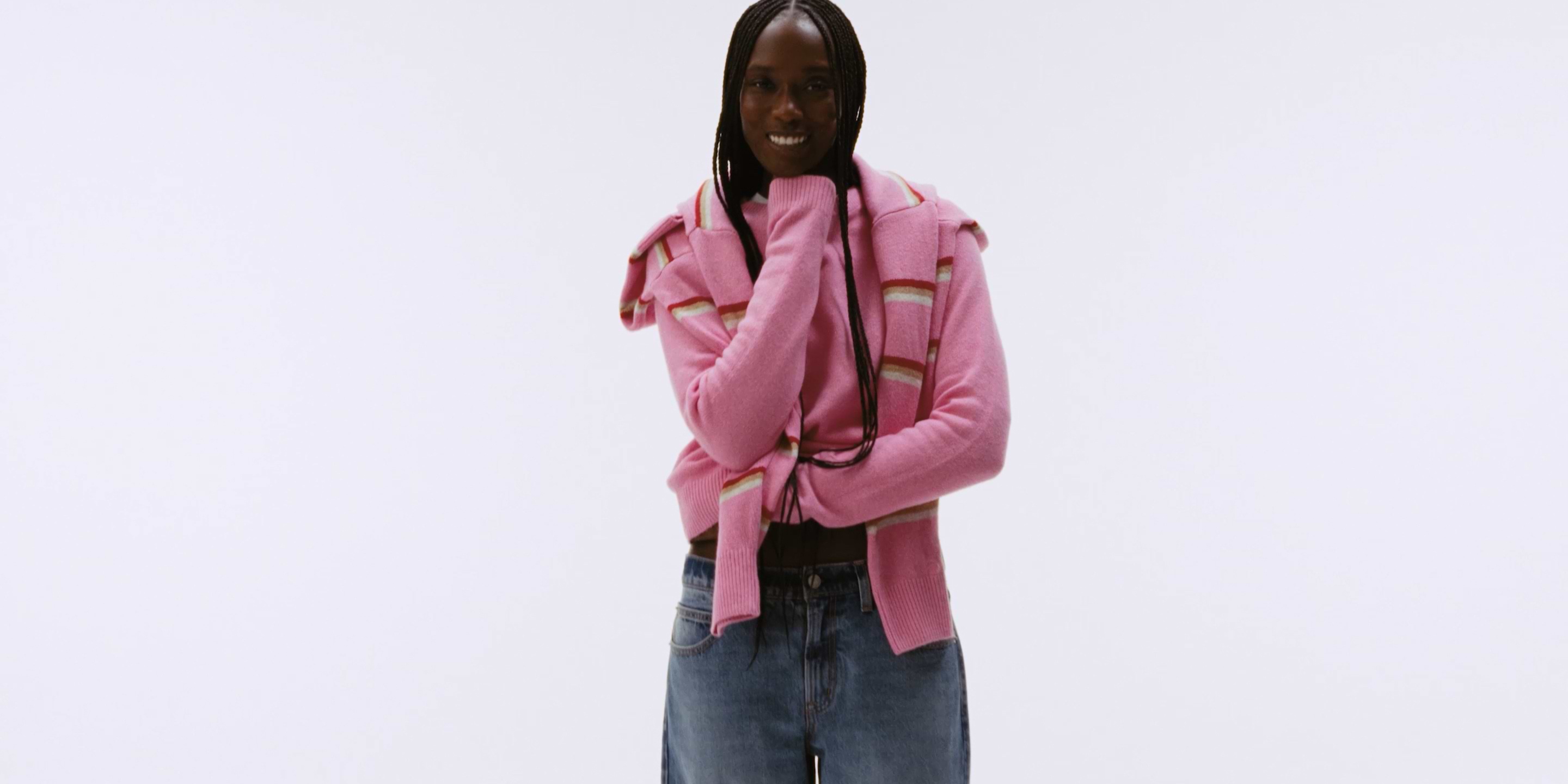 a woman with long hair and a pink sweater is holding her arms out