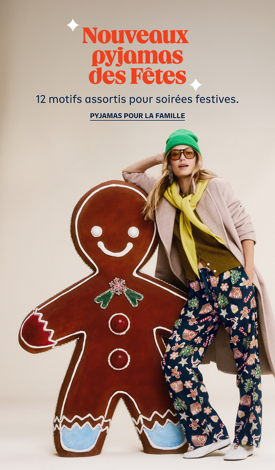 Model in holiday pajama pants and green beanie leans on a giant gingerbread cookie; French text advertises “Nouveaux pyjamas des Fêtes” and family holiday PJs.