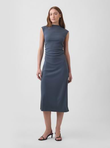 Person wearing a slate-blue, high-neck sleeveless midi dress with black strappy heels against a plain backdrop.