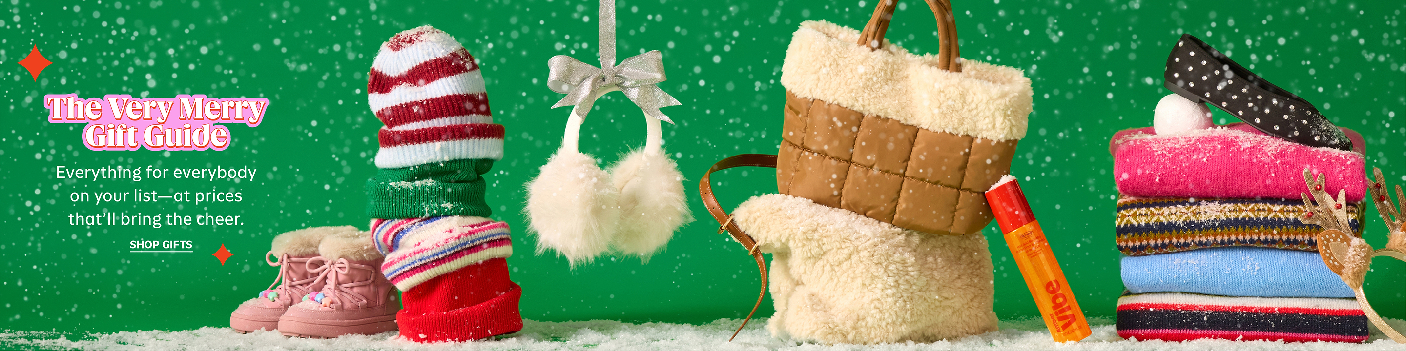 Holiday gift guide display: snow-dusted knit hats, pink fur-lined boots, fluffy earmuffs, shearling tote, and stacked sweaters topped with a studded flat.