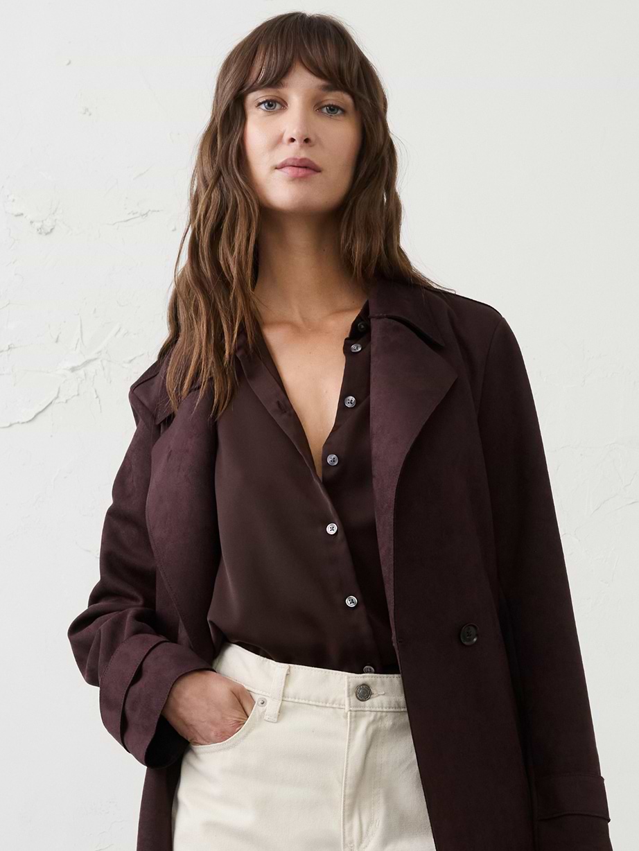 Model in a dark brown coat and blouse with cream jeans, hand in pocket.