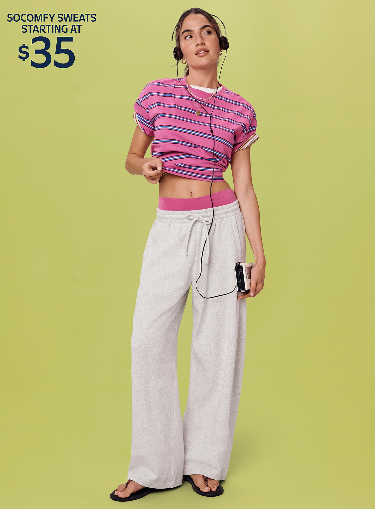 Person in a pink striped crop top and gray wide‑leg sweatpants listens on headphones, holding a cassette player; text reads “Get the look for $45.”
