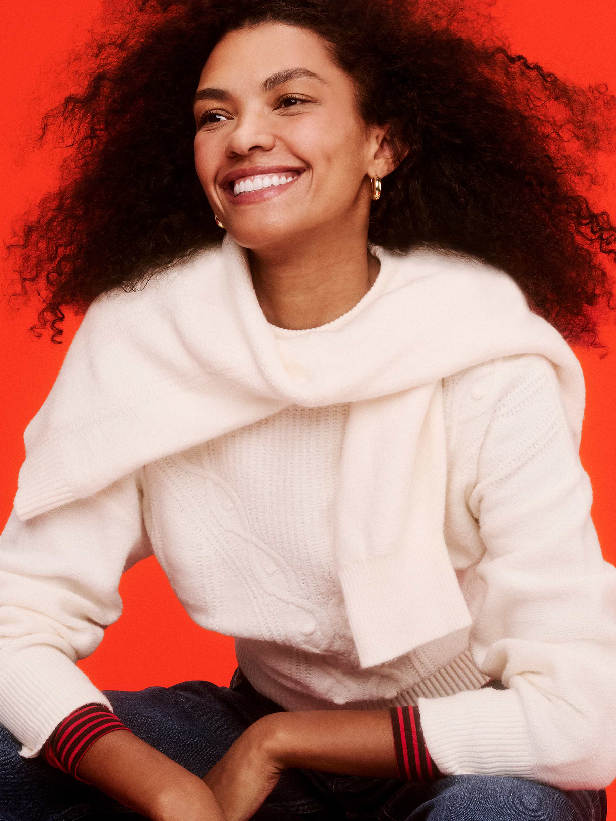 Smiling person in a white knit sweater with a matching wrap, red background; text reads “Sweaters from $29.”