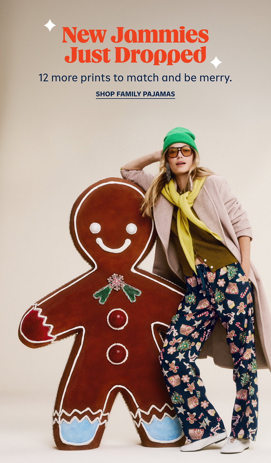 Person in festive pajama pants leans on a giant gingerbread cookie; text reads “New Jammies Just Dropped—12 more prints. Shop family pajamas.”