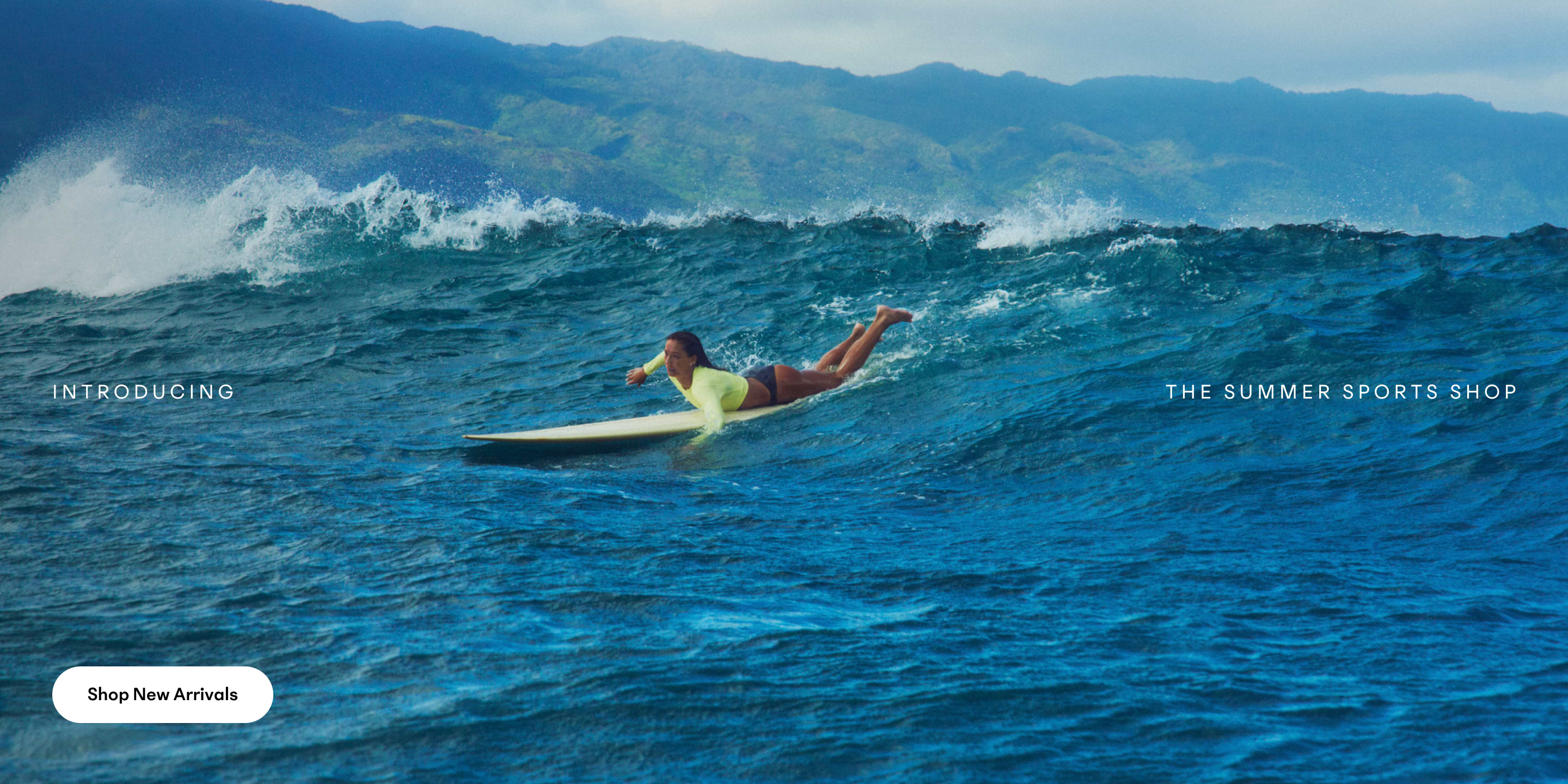 Person paddling a surfboard on choppy blue ocean with distant green mountains.
