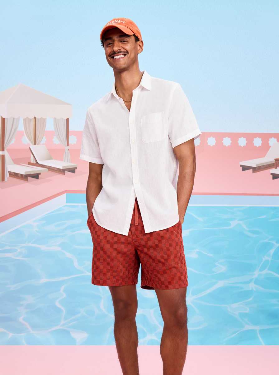 Male model wearing a white button down and orange swim trunks.