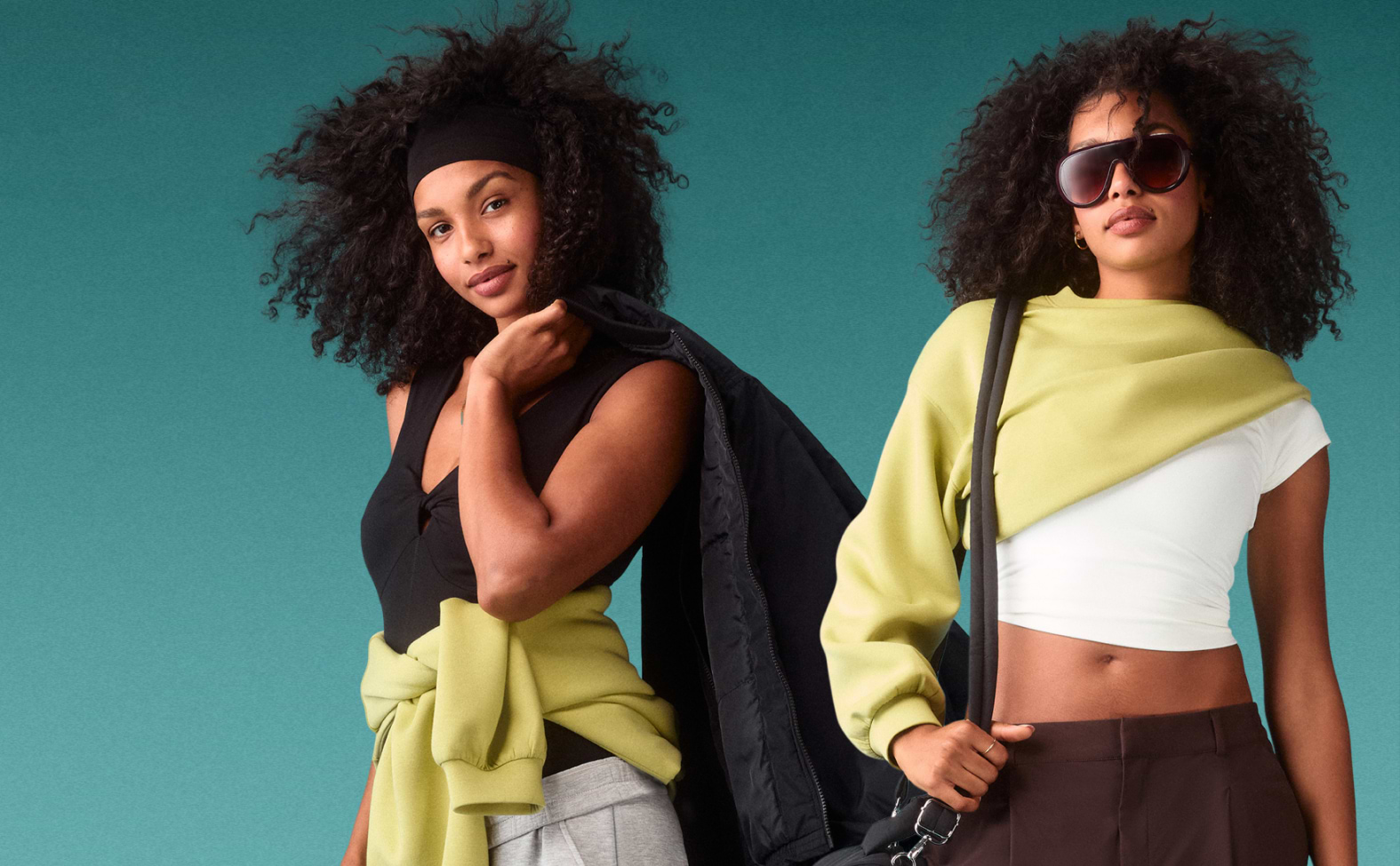 Two models in athleisure pose against a teal backdrop—left in a black top and gray joggers with a green sweatshirt at the waist; right in a white crop top, brown pants, sunglasses, sweatshirt on shoulders.