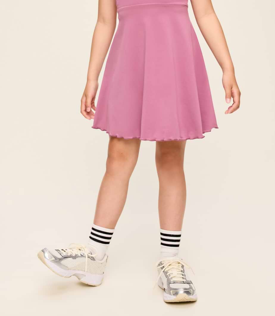 Lower body of a person in a pink flared dress, striped socks, and silver sneakers.
