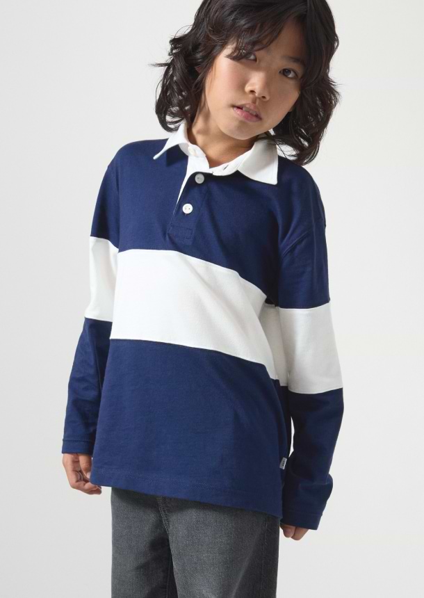Child wearing a navy-and-white color‑block long-sleeve rugby shirt with a white collar and gray jeans against a plain background.