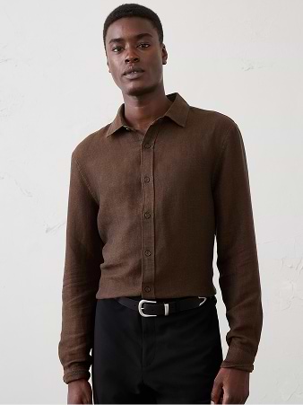 Person wearing a brown long-sleeve button-up shirt and black trousers with a belt, standing against a light wall.