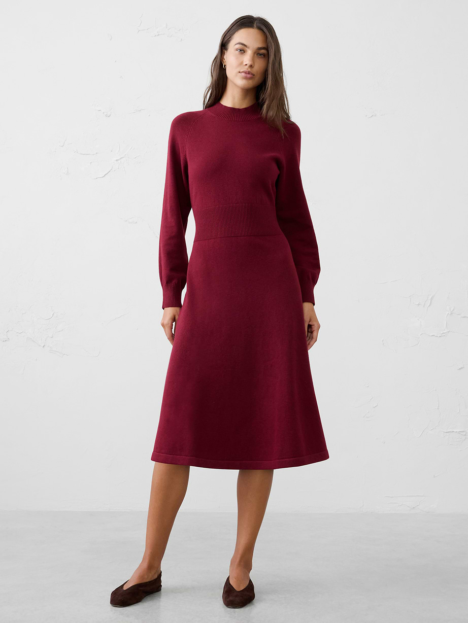 Person wearing a burgundy long-sleeve knit midi dress with a fitted waist, paired with brown flats, standing against a plain white background.