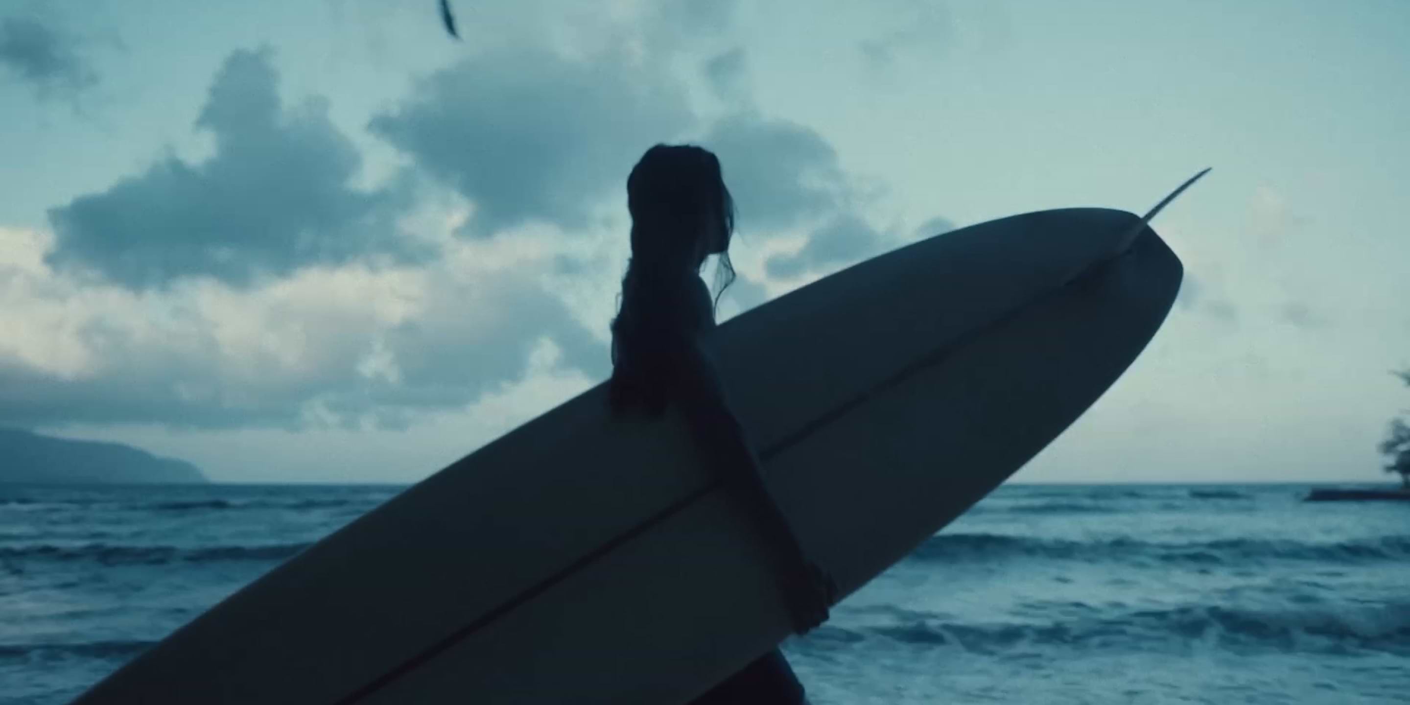 a woman walking on the beach with a surfboard in her hand