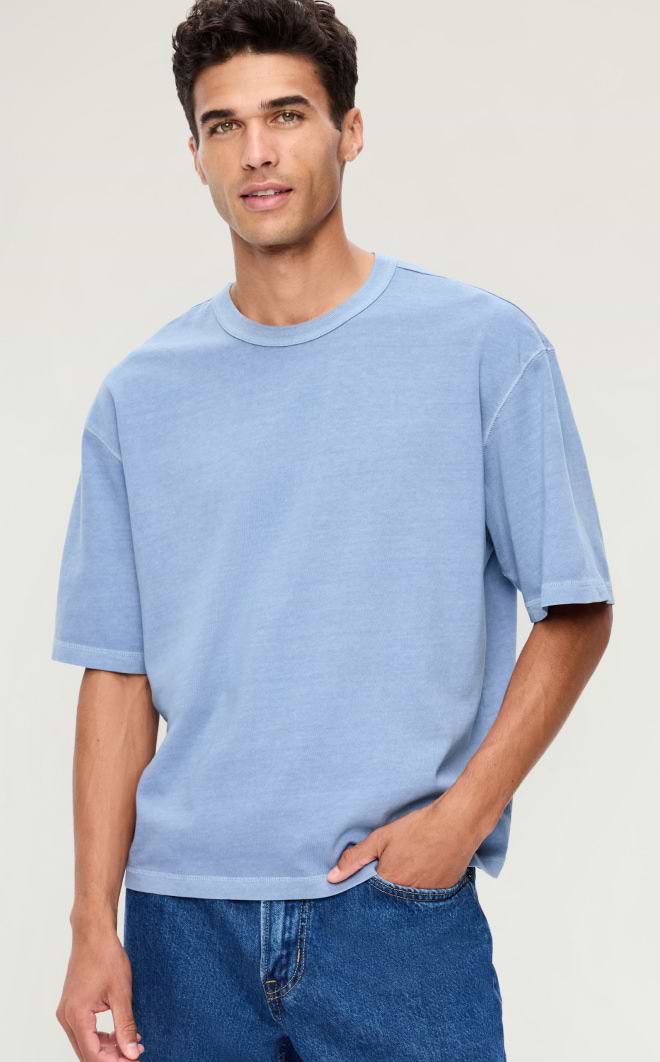 Person in a light blue oversized T-shirt and blue jeans, one hand in pocket, standing against a plain light background.