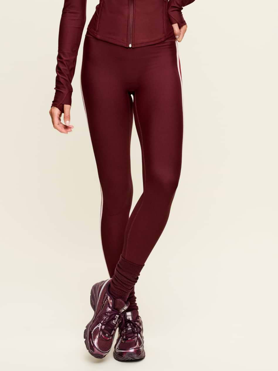 Close-up of legs in burgundy leggings with scrunched socks and matching maroon running shoes against a light background.